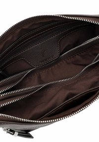 Interno di borsa in pelle marrone con molteplici tasche con cerniera, trama liscia e dettaglio del logo. La fodera è in tessuto marrone scuro.