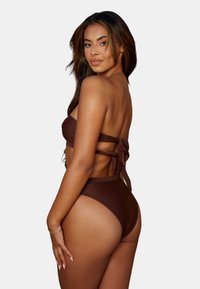 Ensemble de bikini marron composé d'un haut sans bretelles avec un nœud au dos et un bas taille haute. Texture lisse et design simple.