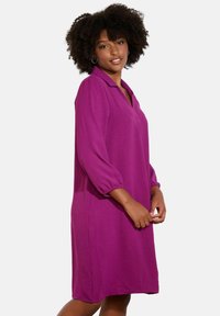 Robe violette avec col, à manches trois-quarts, coupe décontractée, tissu texturé et longueur au genou, présentant une finition lisse.