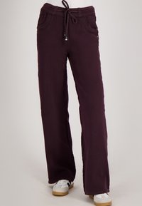 Donkerpaarse wijde broek met voorzakken en een elastische tailleband, gecombineerd met zwart-witte sneakers.