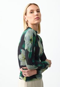 T-shirt à manches longues avec un fond noir orné de grands motifs floraux verts et blancs. Fabriqué à partir d'un tissu lisse et extensible avec une coupe ajustée.