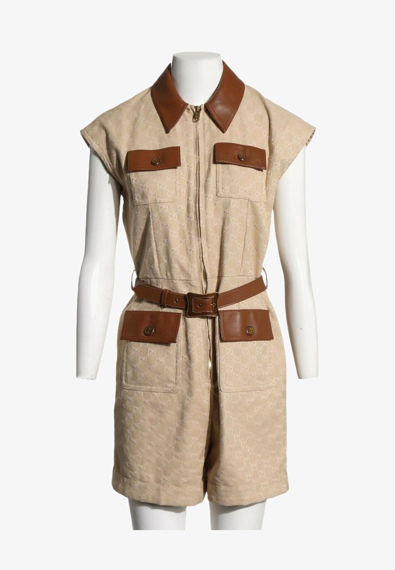 Combinaison beige sans manches avec col en cuir marron, ceinture et quatre poches à rabat avec boutons sur un mannequin blanc.