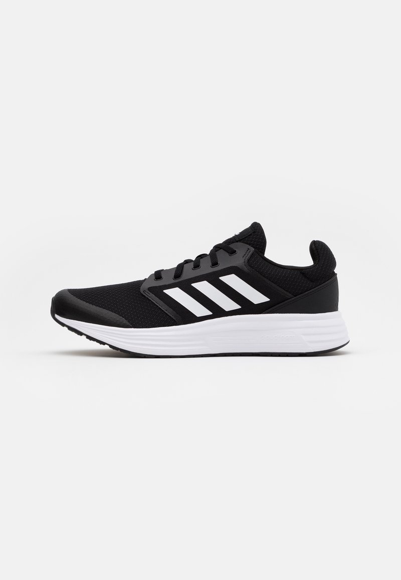 Chaussures de sport noires avec un dessus en mesh, arborant trois rayures blanches sur le côté et une semelle blanche en contraste.