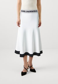 Hvit strikket skjørt med en utvidet design, svart ribbestrikket kant og elastisk liv med "KARL LAGERFELD" logo. Glatt tekstur.
