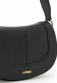 Schwarze Handtasche aus Kunstleder mit einer geschwungenen, strukturierten Form. Mit Akzentnähten und einem goldenen Logo auf der Vorderseite. Glatte Textur.