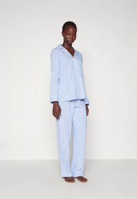 Σετ πιτζάμες με μπλε και λευκές ρίγες, που περιλαμβάνει μπλούζα με κουμπιά και μακρυμάνικα μανίκια και παντελόνι που ταιριάζει. Μαλακό ύφασμα με άνετη εφαρμογή και μανσέτες στα μανίκια.