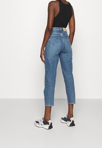 Džíny z modrého denimu s vysokým pasem, fitted siluetou a rovnými nohavicemi. Obsahují dvě zadní kapsy a mírně třepení na lemu.