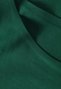 Grüner Stoff mit glatter Textur und leichtem Glanz. Verfügt über einen Rundhalsausschnitt und genähte Kanten, zeigt eine einfarbige Oberfläche ohne Muster.