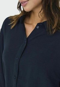 Navy blue button-up shirt with a textured fabric, featuring a collar and a partial placket with dark buttons.