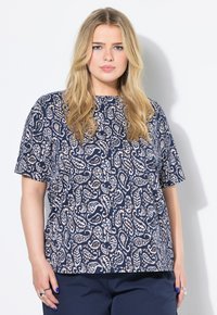 Námořnická modrá blůza s paisley vzorem v bílé a béžové barvě, s krátkými rukávy a kulatým výstřihem, doplněná námořnickými kalhotami.