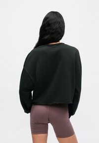 Μαύρο cropped φούτερ με χαλαρή εφαρμογή, στρογγυλή λαιμόκοψη και εμφανείς ραφές, σε συνδυασμό με εφαρμοστά ροζ ποδηλατικά σορτς σε σκόνη.