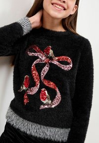 Maglione nero peloso con motivi di nastri decorati con paillettes rosse e rosa, dettagli ricamati e polsini a coste grigi all'orlo.
