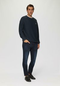 Marineblaues Sweatshirt mit Rundhalsausschnitt und strukturiertem Stoff, kombiniert mit dunkelblauen Slim-Fit-Jeans und schwarzen Sneakers.