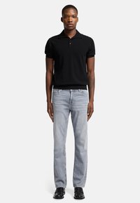 Polo shirt nera a maniche corte con colletto piatto, abbinata a jeans dritti blu chiaro e scarpe nere. Un outfit semplice e casual.