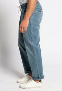 Pantalones de mezclilla azul claro con un corte relajado, cinturilla elástica y puños doblados, combinados con zapatillas blancas. Diseño simple y funcional.