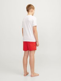 Maglietta bianca a maniche corte abbinata a pantaloni corti rossi brillanti, caratterizzata da un design semplice e una texture uniforme. Nessun motivo o accento visibile.