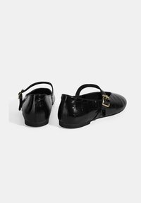 Schwarze Leder-Ballerinas mit Kroko-Textur, ausgestattet mit einem Mary-Jane-Riemen und einer goldenen Schnalle. Flache Sohlen und runde Zehen.