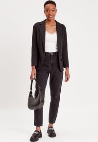 Blazer noir, débardeur en dentelle blanche, jeans noirs taille haute, sac à main texturé noir, mocassins épais avec un accent en chaîne.