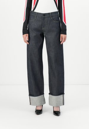 Wide-leg dark denim jeans with turned-up gray cuffs. Features a button closure, visible stitching, and falls over black heels.