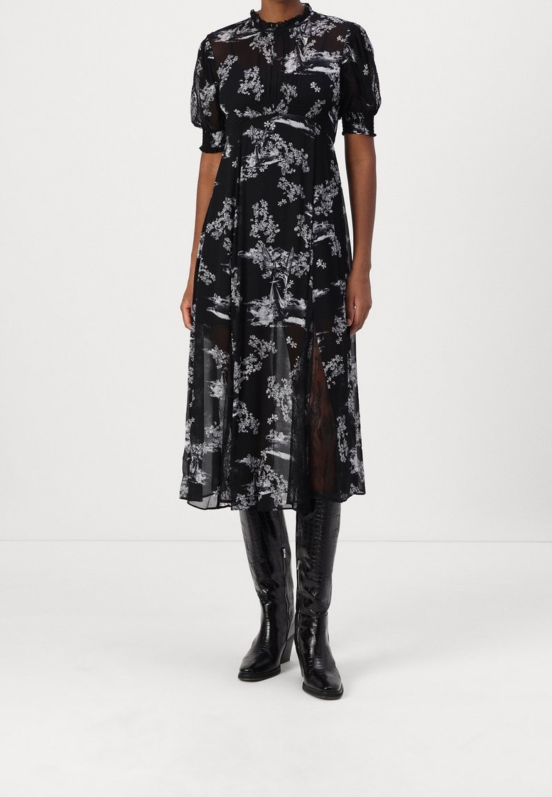 Robe midi noire avec imprimé floral blanc, manches bouffantes transparentes, col montant, fente à l'avant, associée à des bottes noires montantes jusqu'au genou.