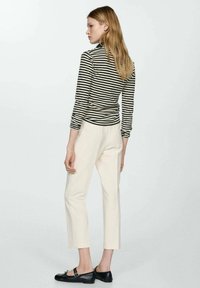 Blusa de rayas negra y blanca de manga larga, pantalones crema ajustados y zapatos planos negros. Diseño simple con una silueta ajustada y acentos mínimos.