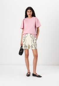 Haut rose à manches courtes avec épaules froncées, associé à un short crème arborant un motif abstrait noir, complété par des accessoires noirs.
