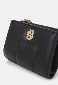 Portefeuille en cuir noir avec un logo doré, fermeture zippée et un panneau texturé, forme rectangulaire compacte avec une finition lisse.
