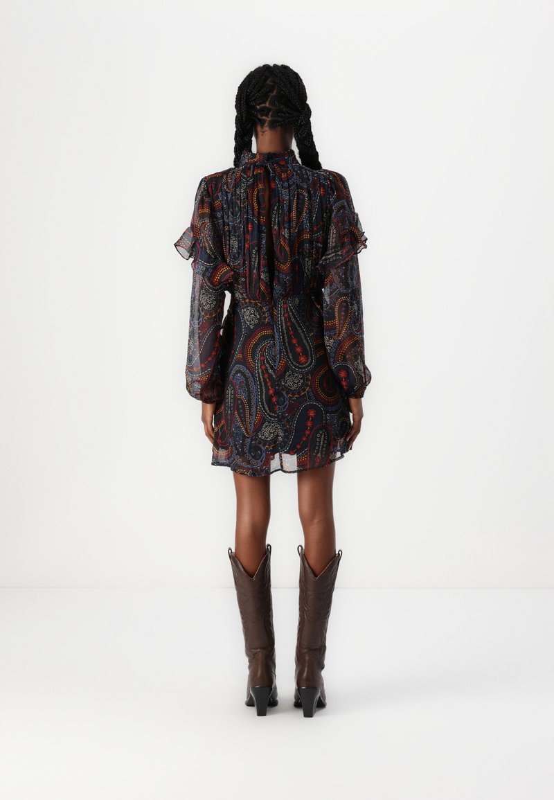 Vestido de manga larga en tela oscura con estampado paisley, acentos con volantes en los hombros, cintura ajustada y falda en capas; combinado con botas marrones de punta.