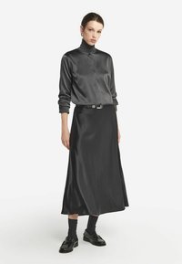 Grå satin långärmad skjorta med hög krage, i kombination med en matchande flödande kjol. Outfiten har ett bälte med en metallspänne och svarta skor.