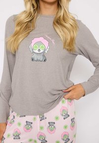 Gray long-sleeve top with a cartoon dog wearing a pink towel and cucumber slices. Light pink pants featuring similar dog illustrations in a repeating pattern.