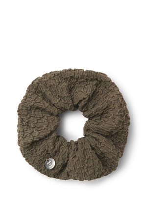 Coletero marrón tejido con un patrón texturado y pequeñas motas metálicas, con una etiqueta redonda plateada en un lado.