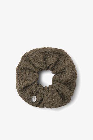 Coletero marrón tejido con un patrón texturado y pequeñas motas metálicas, con una etiqueta redonda plateada en un lado.