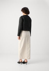 Maglione corto nero a trama, gonna lunga color crema e mules neri con tacco. Tessuto morbido, design semplice e estetica minimalista.