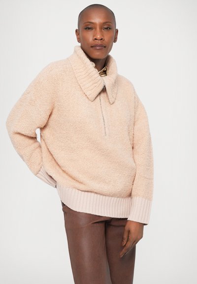 Pullover rosa chiaro e morbido con alto colletto, dettaglio con zip e orlo a costine. Le maniche lunghe e la vestibilità rilassata completano la morbidezza della texture.
