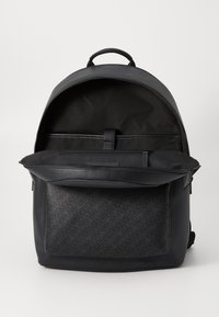 Black backpack with a textured front panel, zippered main compartment, and smooth leather accents. Features a top handle and adjustable straps.