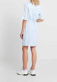 Jasnoniebieska sukienka do kolan, krótki falbaniasty rękaw, elastyczna talia, gładki materiał, noszona z białymi butami sportowymi, prosty fason.
