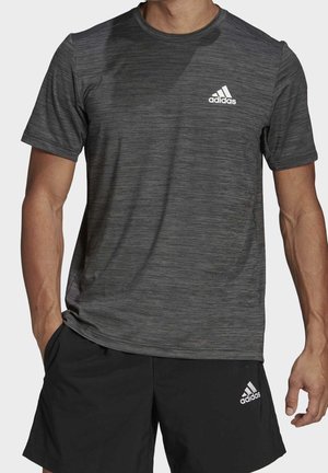 Mężczyzna ubrany w ciemnoszarą koszulkę Adidas z krótkim rękawem i czarne spodenki Adidas z logo na lewej piersi i lewym udzie.