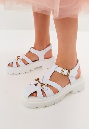 Witte platform sandalen met dikke zolen, voorzien van kruislings gevlochten bandjes en een gouden gespaccent. Glad textuur, open teen ontwerp.
