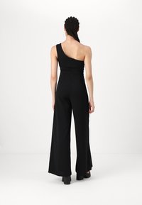 Svart jumpsuit med en axel, åtsittande överdel, vida byxor och strukturerad tyg med döljd dragkedja i ryggen.