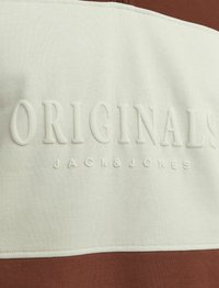 Pamut pulcsi, három vízszintes csíkban krém és rozsdabarna színben, dombornyomott "ORIGINALS JACK&JONES" felirattal a felső csíkon.