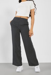 Pantalon large à pois noirs et blancs avec une taille élastique, associé à un top court blanc ajusté et des baskets blanches.