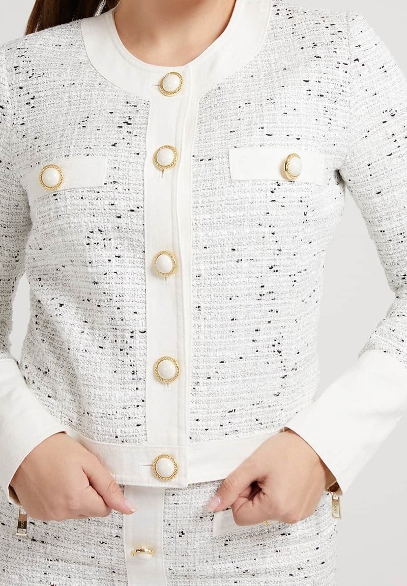 Vit tweedjacka med svarta inslag, försedd med knappar i guldton och framfickor. Tyg med struktur, figursydd silhuett och krage.