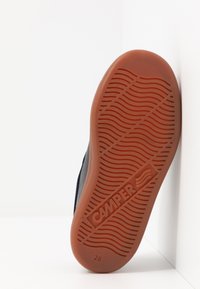 Apavu zole ar teksturētu gumiju oranžā krāsā, ar viļņotu protektora rakstu un "CAMPER" logotipu. Pievienota tumšai auduma virsmai brīva dizaina stilā.