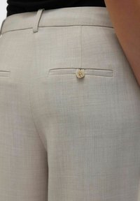 Lichtbeige op maat gemaakte broek van textuurstof, met een achterzak met een knoopsluiting en een gladde tailleband.