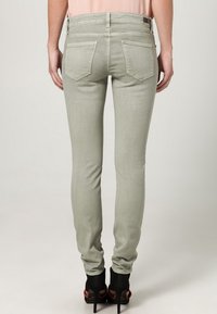 Jeans ajustados color gris claro de denims, con bolsillos traseros y una textura suave, combinados con zapatos de tacón negro.