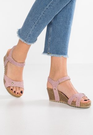 Pies con sandalias de cuña rosa texturizadas con suelas de corcho y correas en los tobillos, combinadas con vaqueros azules con el dobladillo deshilachado.