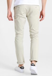 Pantaloni beige slim-fit con una texture liscia, due tasche posteriori e risvolti, abbinati a sneaker bianche con marchio nero.