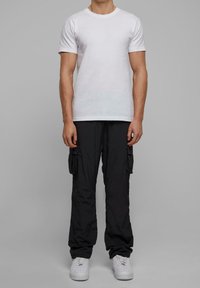 Bílé tričko s krátkým rukávem spojené s černými cargo kalhotami s velkými bočními kapsami, doplněné bílými teniskami.