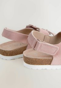 Roze suède sandalen met een kurken zool, verstelbare band en witte rubberen loopzool. Heeft een ronde teen en een getextureerde voetbed.