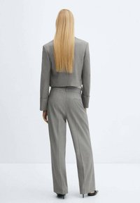 Blazer gris a medida con diseño corto, combinado con pantalones anchos grises. Tela suave, detalles mínimos de costura y líneas limpias.